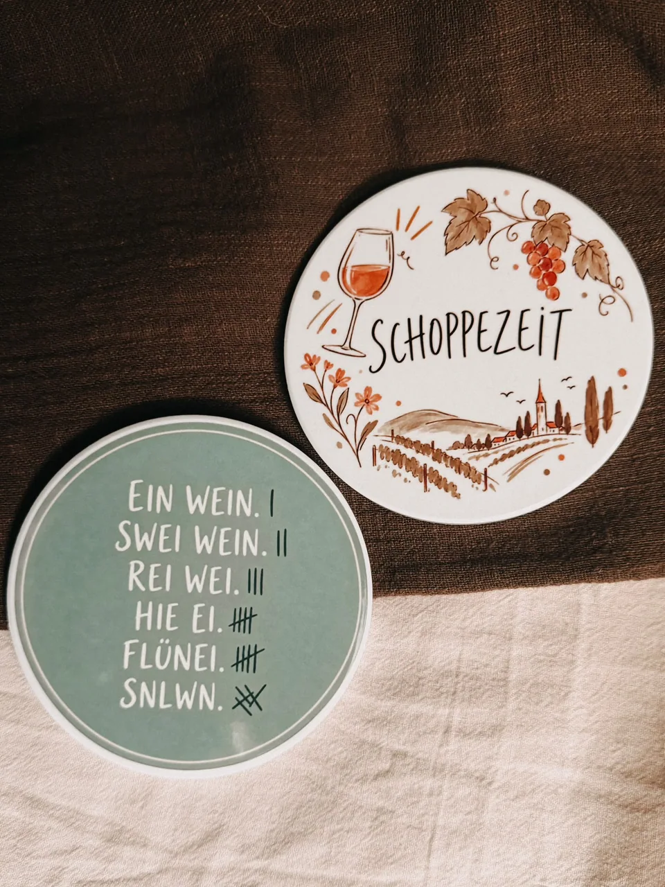 Zwei runde Keramik-Untersetzer mit Weinmotiven und Sprüchen