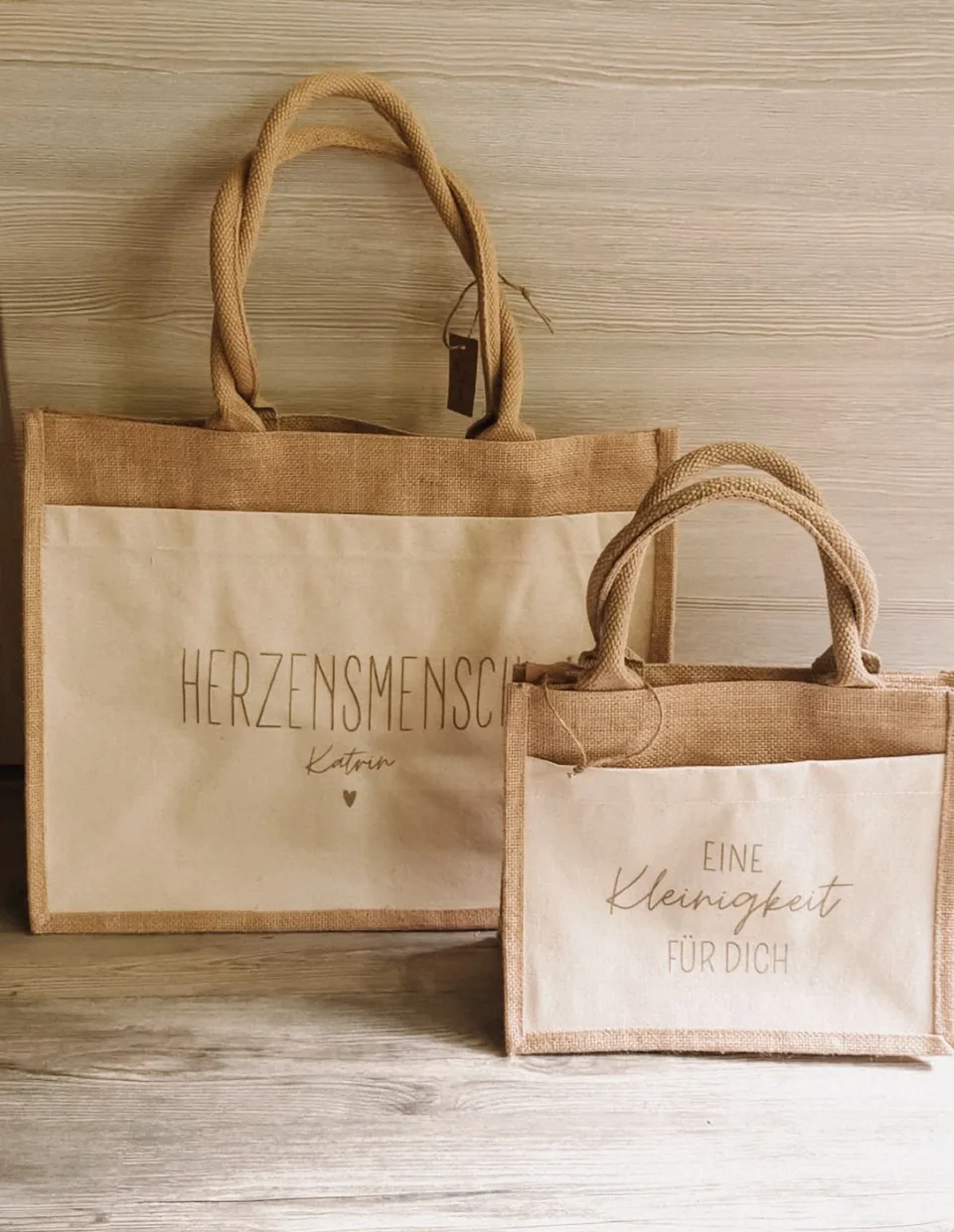 Kleine Jutetasche mit der Aufschrift „Eine Kleinigkeit für dich“ vor einem größeren Shopper